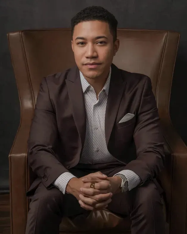 Portrait of Michael Keyes, MD, seated in a leather armchair and wearing a brown suit